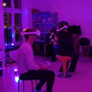 Zwei sitzende Personen mit VR-Brille in lila beleuchtetem Raum