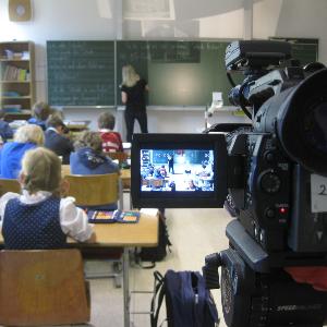 Foto einer Unterrichtsaufzeichnung mit Kamera im Fokus und Schulklasse im Hintergrund