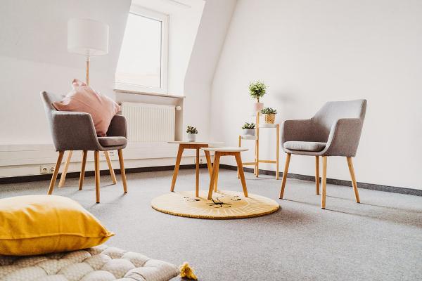 Therapieraum mit zwei Sesseln, einem Tisch, einem Sitzkissen, Teppich und Pflanzen