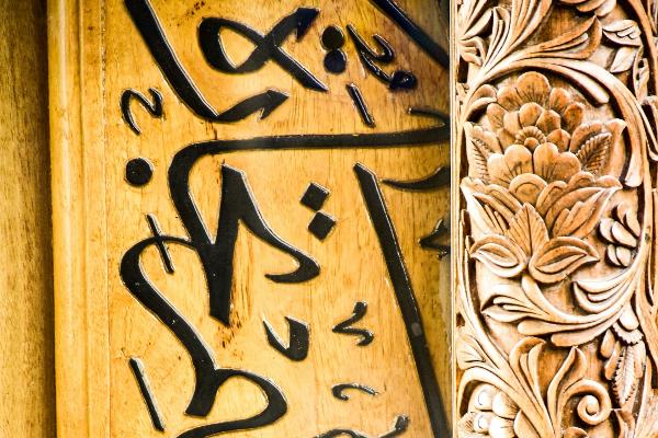 Arabische Schrift auf gelbem Holz mit einer Zierleiste rechts.