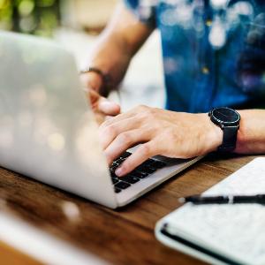 Person, die vor einem Laptop sitzt und darauf tippt.