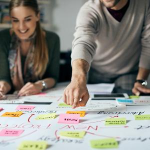 Gruppe junger Menschen über eine Tafel mit Post-its gebeugt