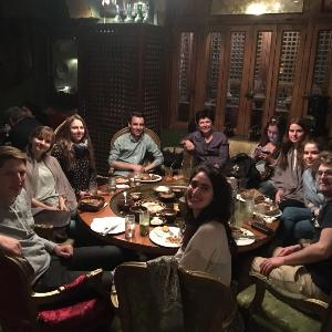 Gruppe Studierender, die um einen runden Tisch herum beim Abendessen sitzen.