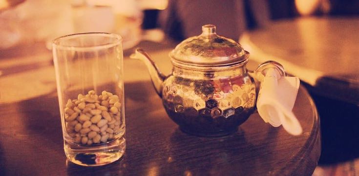 Teekanne im orientalischen Design. Daneben ein Glas mit Pistazienkernen.
