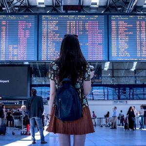 Frau am Flughafen vor der Tafel mit Abflügen