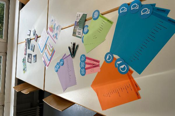 Table covered with coloured cards displaying linguistic landscape taxonomies, together with pens and workshop materials. The activity supports collaborative discussion and hands-on engagement with methods of linguistic landscape research.