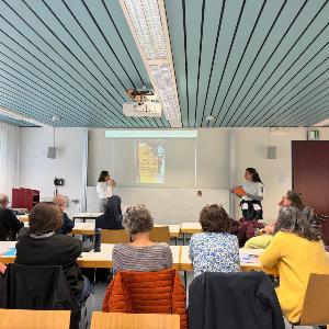 Studierende nehmen an einer Seminarveranstaltung teil, während zwei Teilnehmerinnen Ergebnisse vor der Gruppe präsentieren. Die Aufnahme zeigt gemeinsames Lernen, Diskussion und Präsentation im universitären Unterricht.