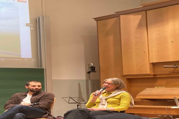 Nahaufnahme der Bühne auf zwei sitzende Personen, die diskutieren, eine Person hält ein Mikro