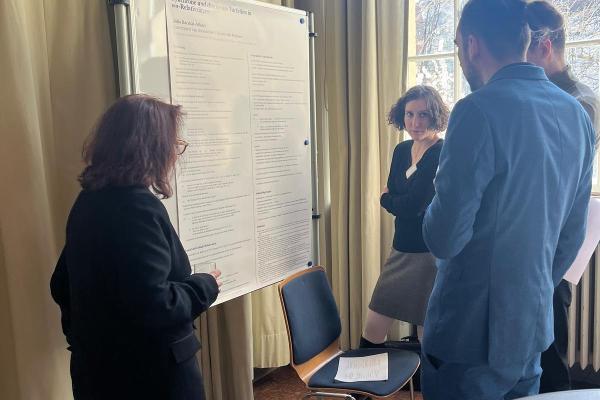 Vier Personen stehen vor einem Poster und schauen es sich an