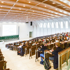 Large auditorium filled with students during a lecture, with a green decorative watermark