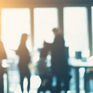 Silhouettes of people walking and talking in a bright office building. | © iStock Silhouettes of people walking and talking in a bright office building.