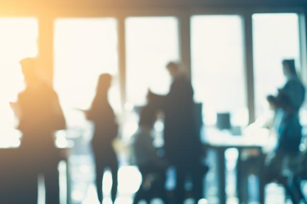 Silhouettes of people walking and talking in a bright office building.