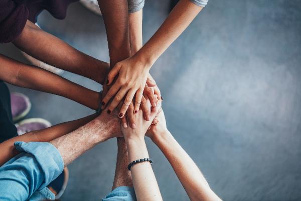 Several hands placed together in a gesture of teamwork and unity, symbolizing collaboration and joint research effortts