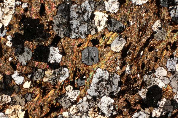 Rock thin section with grey larger minerals in a colourful groundmass