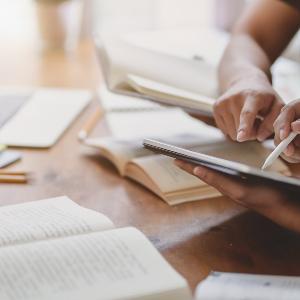 Symbolbild: Zwei Personen arbeiten mit Büchern, PC und Tablet.