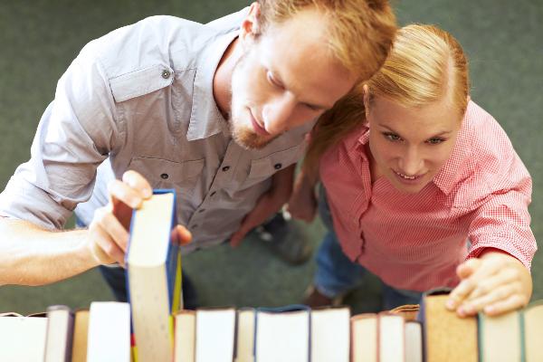 Symbolbild: Eine junge Frau und ein junger Mann nehmen ein Buch aus dem Regal.