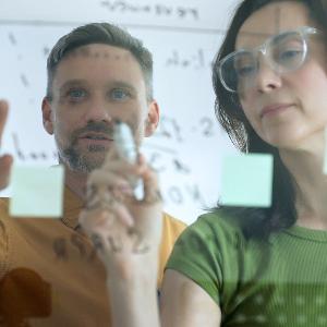 Symbolbild: Eine Frau und ein Mann schreiben auf eine Glaswand