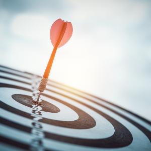 Symbolbild: Ein roter Dartpfeil steckt in der Mitte einer Dartscheibe.