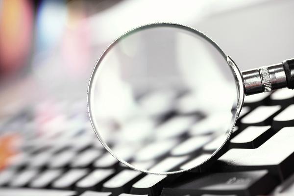 Symbolbild: Eine Lupe vergrößert eine Computertastatur.