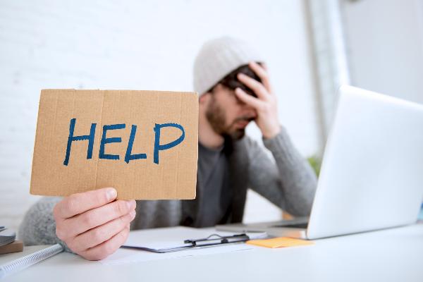 Symbolbild: Junger Mann hält Schild mit Aufschrift Help in die Kamera.