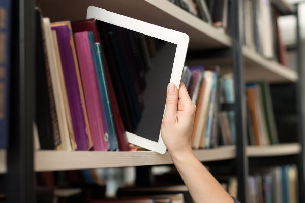 Symbolbild: Eine Person zieht ein Tablet aus einem Bücherregal.