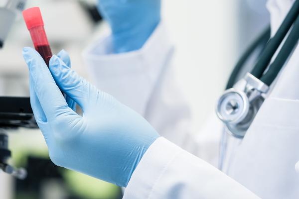 A person with a labcoat and protective gloves looks through a microscope