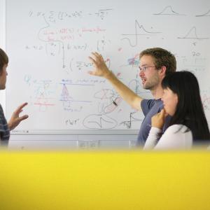 Personen stehen an einer Tafel und erklären sich gegenseitig etwas. | © LMU / Jan Greune Personen stehen an einer Tafel und erklären sich gegenseitig etwas.
