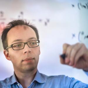 Prof. Dr. Til Birnstiel zeichnet etwas an eine gläserne Scheibe