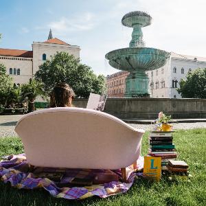 Eine Studentin liest auf einer Couch vor dem Brunnen am Geschwister-Scholl-Platz ein Buch.