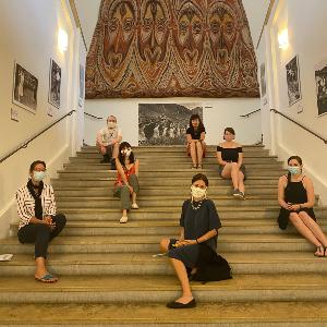Studierende sitzen mit der Dozentin Krämder de Huerta auf einer Treppe im Museum Fünf Kontinente