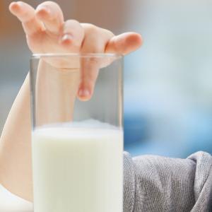 Ein Kind steckt den Finger in ein Milchglas.