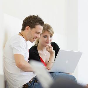 Studierende sitzen vor einem Laptop und unterhalten sich.