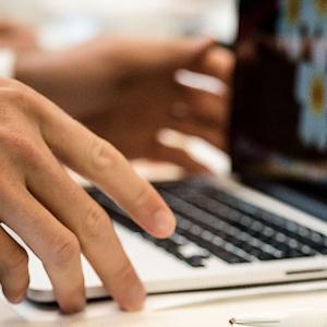 Eine Person arbeitet an einem Laptop, daneben liegt eine Infobroschüre der LMU.