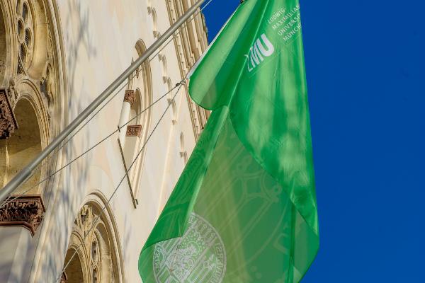Grüne Flagge mit dem Logo der LMU an einem Gebäude