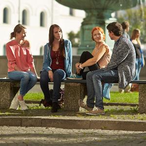 Studierende sitzen am Brunnen vor dem Hauptgebäude der Universität.