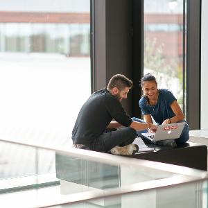 Studierende unterhalten sich vor einem Laptop.