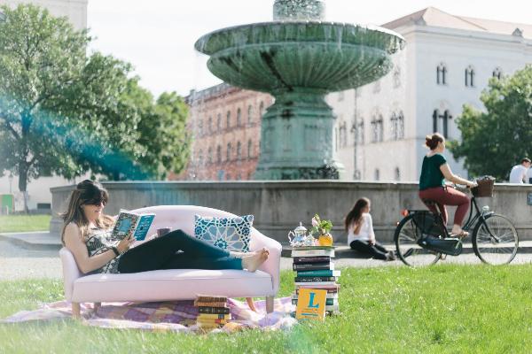 Eine Studentin liest auf einer Couch vor dem Brunnen am Geschwister-Scholl-Platz ein Buch.