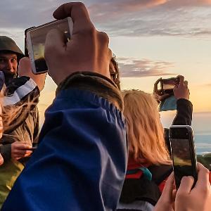 Einige Personen fotografieren den Sonnenaufgang auf dem Gipfel des Berges Geigelstein.