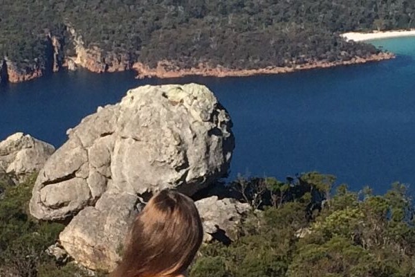 Eine Studentin sitzt auf einem Fels und blickt auf eine Bucht in Australien