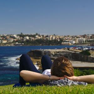 Ein Student entspannt auf einer Wiese in Australien mit Blick auf das Meer.