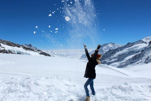 Eine Studentin wirft inmitten von Bergen Schnee in die Luft.