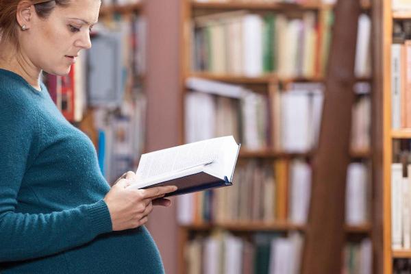 Schwangere Studentin liest vor einem Bücherregal