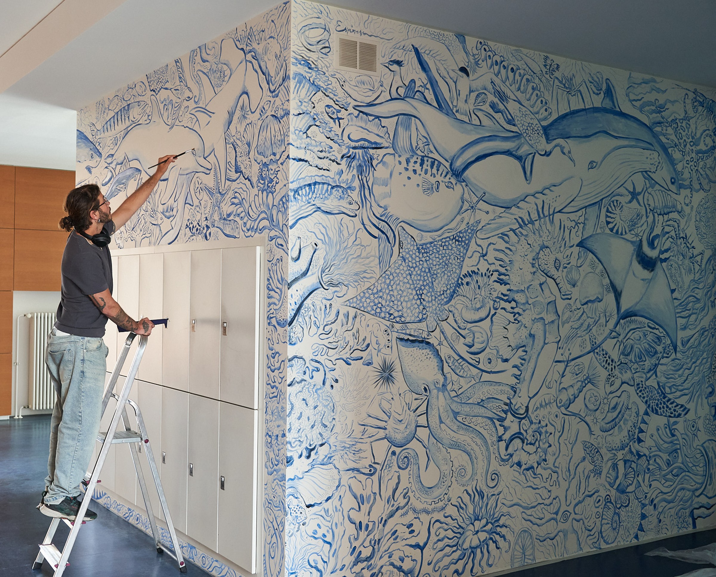 The artist Javier Espinosa is standing on a ladder, painting the upper sections of the mural at LMU´s Biozentrum.