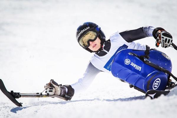 Anna Schaffelhuber in adaptive skiing gear carving through snow on a mono-ski during a winter sports event.