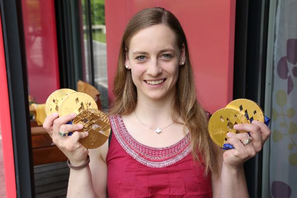 Anna Schaffelhuber in a red top proudly holding multiple gold medals in front of a modern background.