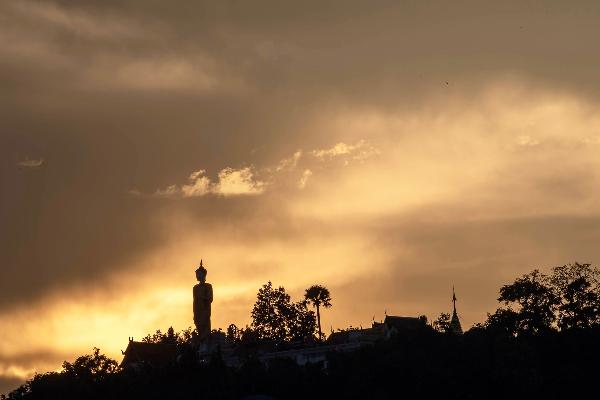 The picture shows a Buddha statue on a hill. The light of the setting sun can be seen behind here.