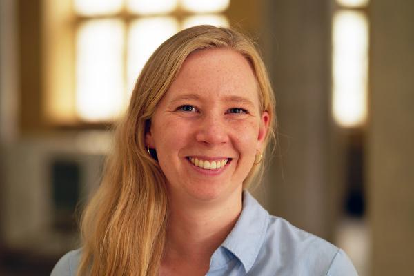 Porträt von Dr. Charlotte Wendland, lächelnd mit hellblauer Bluse in einem modernen, lichtdurchfluteten Innenraum.