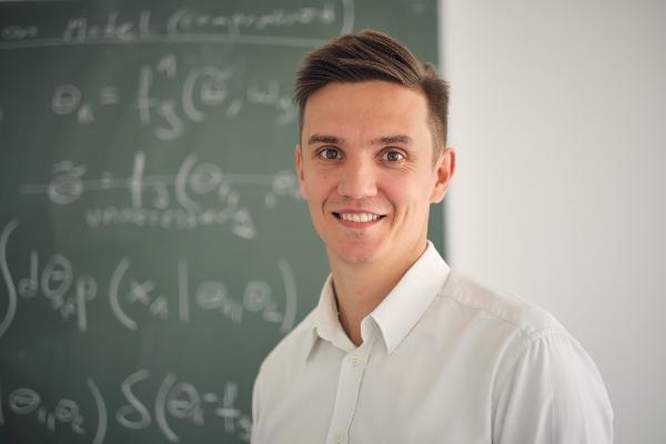 Portrait von Prof. Mlynarski. Er steht vor einer Tafel mit vielen Formeln.