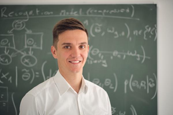 Portrait von Prof. Mlynarski. Er steht vor einer Tafel mit vielen Formeln.