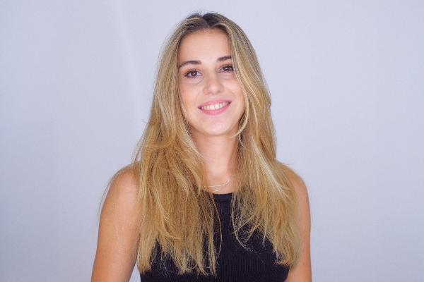 Paulina Leininger, lächelnd, mit langen blonden Haaren, schwarzem ärmellosem Top und natürlichem Make-up vor hellem Hintergrund